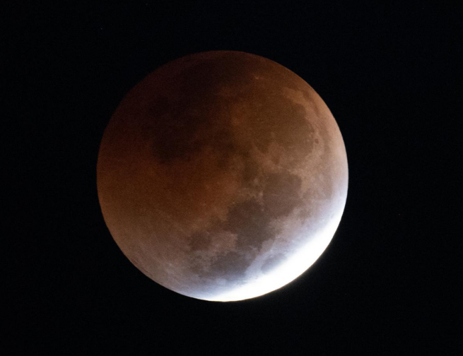 The full Moon appears covered by a dark reddish-grey shadow during a total lunar eclipse.