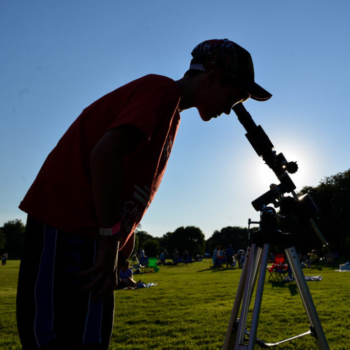 A person looks through a solar observing telescope in a park on a sunny day.